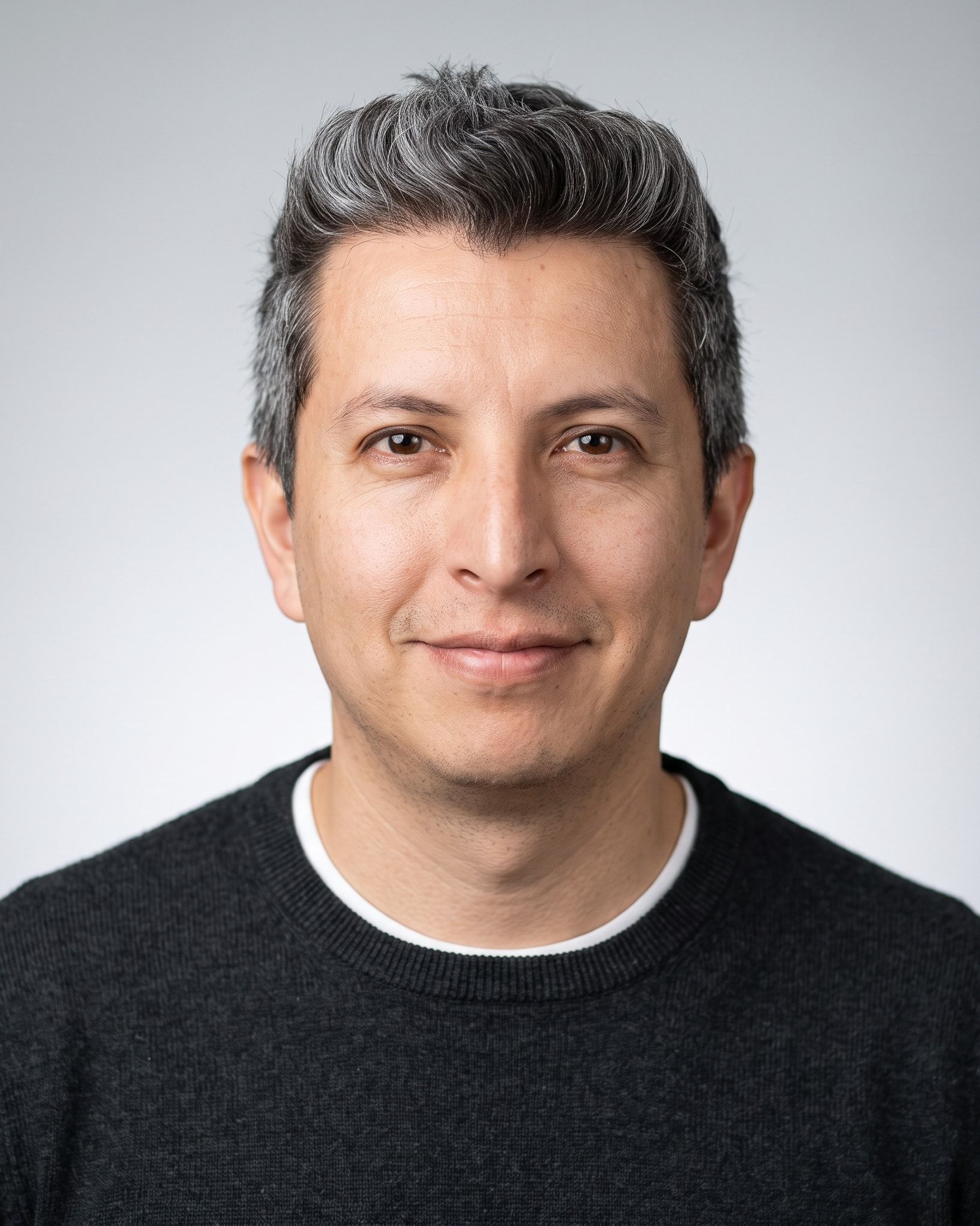 Portrait of Washington X. Quevedo, smiling, wearing a dark sweater against a light gray background